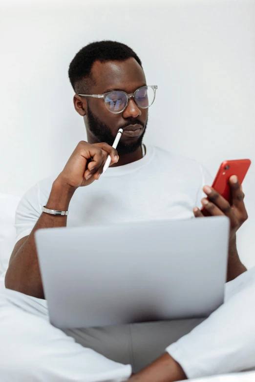 a man sitting on a bed with a laptop and a cigarette in his mouth, trending on pexels, afro tech, white reading glasses, tinder profile, multicoloured