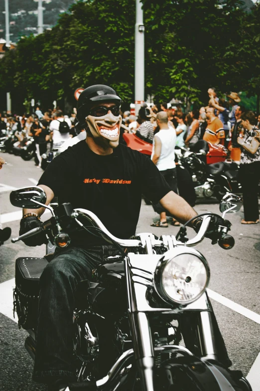a man riding on the back of a motorcycle down a street, pexels contest winner, lowbrow, smiling for the camera, black bandana mask, in front of a large crowd, 🚿🗝📝