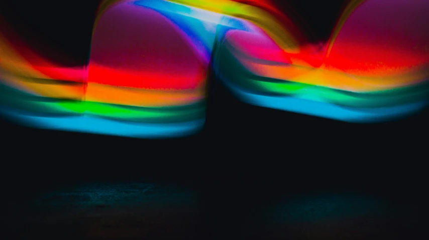 a pair of colorful shoes sitting on top of a black surface, inspired by Bruce Nauman, unsplash, holography, long exposure photo, abstracted, colourful close up shot, color light waves