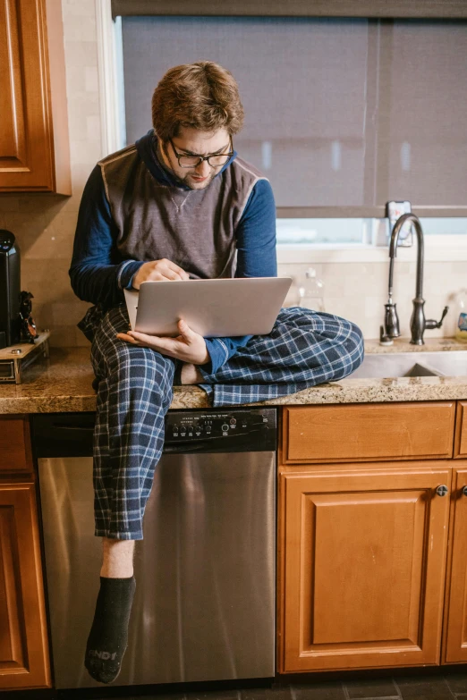 a woman sitting on a kitchen counter using a laptop, by Alexander Brook, pexels, renaissance, wearing a baggy pajamas, plaid tights, handsome man, large pants