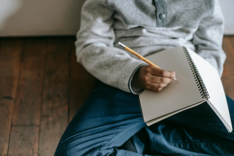 a person sitting on the floor with a notebook and pencil, by Nina Hamnett, pexels contest winner, aged 13, grey, casually dressed, no text