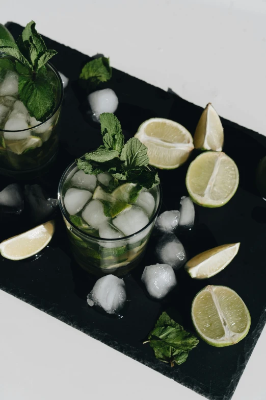 two glasses of mojita sitting on top of a black tray, by Carey Morris, pexels, greens, 🐿🍸🍋, ice cubes, background image