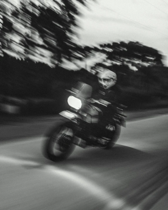 a man riding on the back of a motorcycle down a street, a black and white photo, unsplash, blurry face, late evening, racing, instagram post