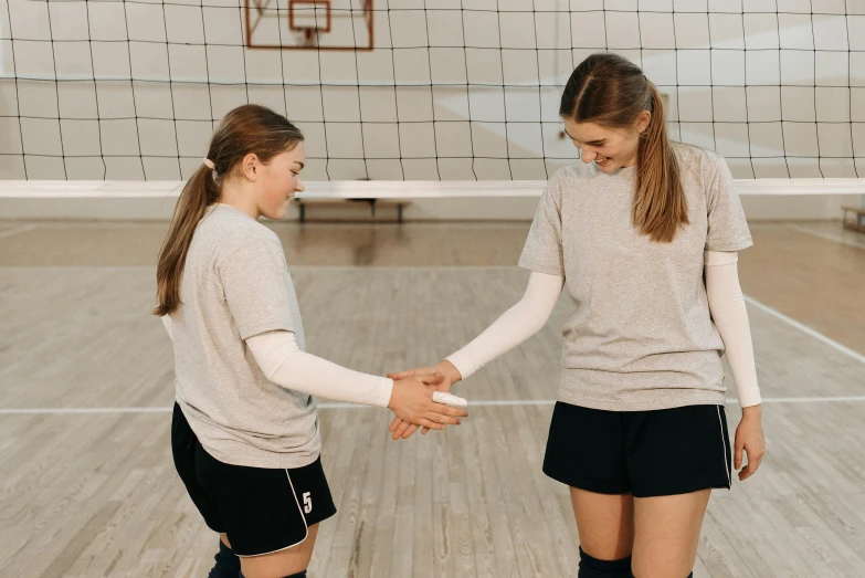 two girls shaking hands on a volleyball court, by Emma Andijewska, unsplash contest winner, renaissance, background image, aged 13, indoor setting, various posed
