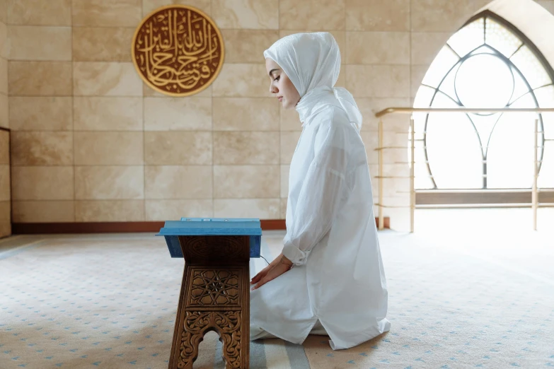 a woman sitting on the floor in a mosque, shutterstock, hurufiyya, wearing lab coat and a blouse, holy ceremony, sitting on a stool, girl wearing hoodie