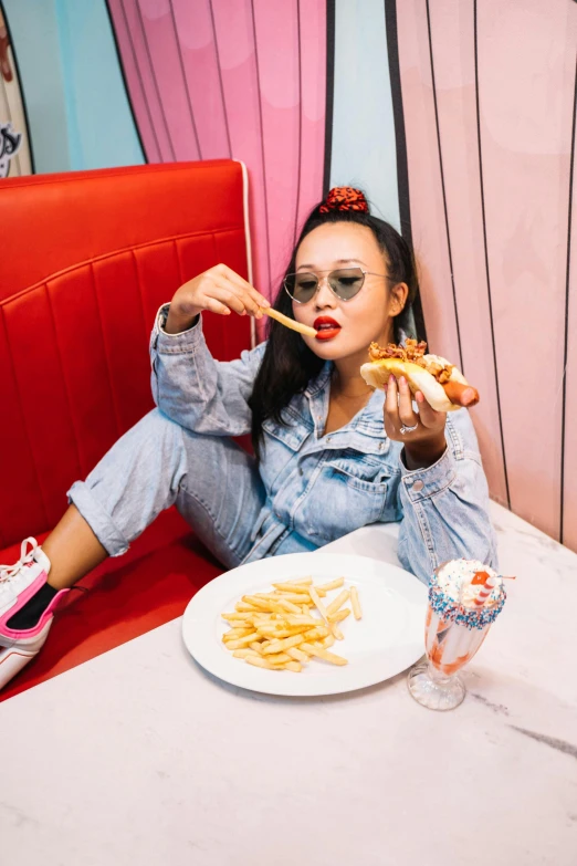 a woman sitting at a table with a plate of food, inspired by Pia Fries, trending on pexels, pop art, blue long pants and red shoes, hot dog, louise zhang, rockabilly style