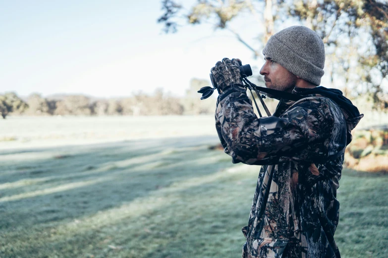 a man that is standing in the grass with a camera, hunters gear, lachlan bailey, looking out, close-up imagery