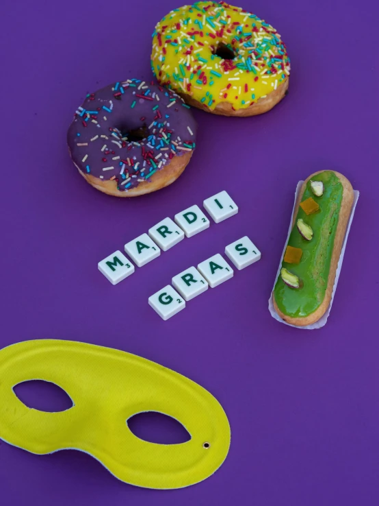 a couple of doughnuts sitting on top of a purple surface, green letters, candy decorations, new orleans, product shot