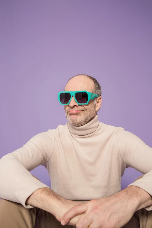 a man sitting on the ground with a pair of sunglasses on his head, a colorized photo, inspired by Leo Leuppi, trending on pexels, bald patch, green and purple studio lighting, subreddit / r / whale, wearing turtleneck