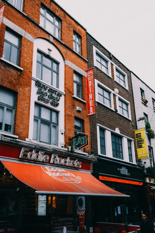 a couple of buildings that are next to each other, by Nick Fudge, trending on unsplash, art nouveau, awnings, pub, vibrant but dreary orange, very busy place