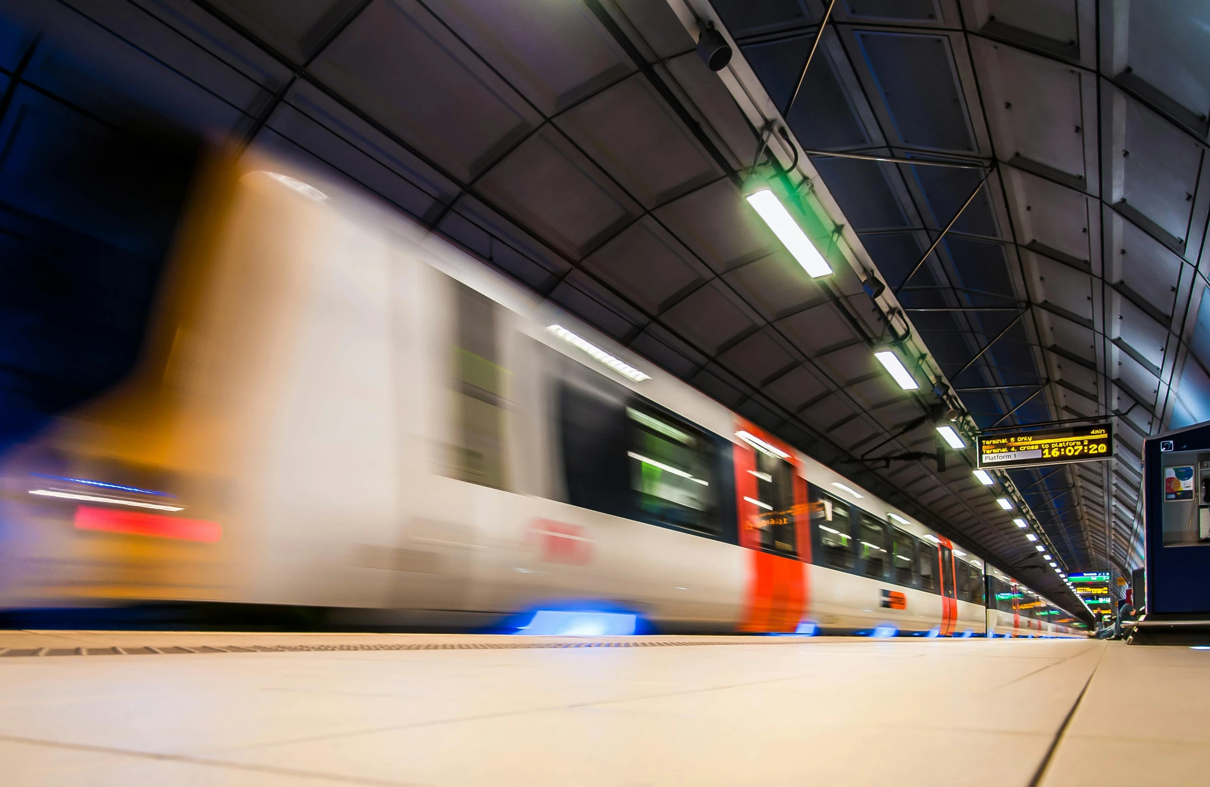 a train traveling through a train station next to a platform, unsplash, speeding through london, whirling gasses, orange line, under light