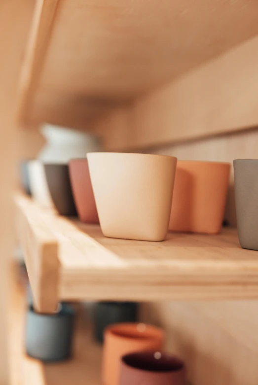 a row of cups sitting on top of a wooden shelf, detailed product image, muted colors. ue 5, soft rubber, detail shots