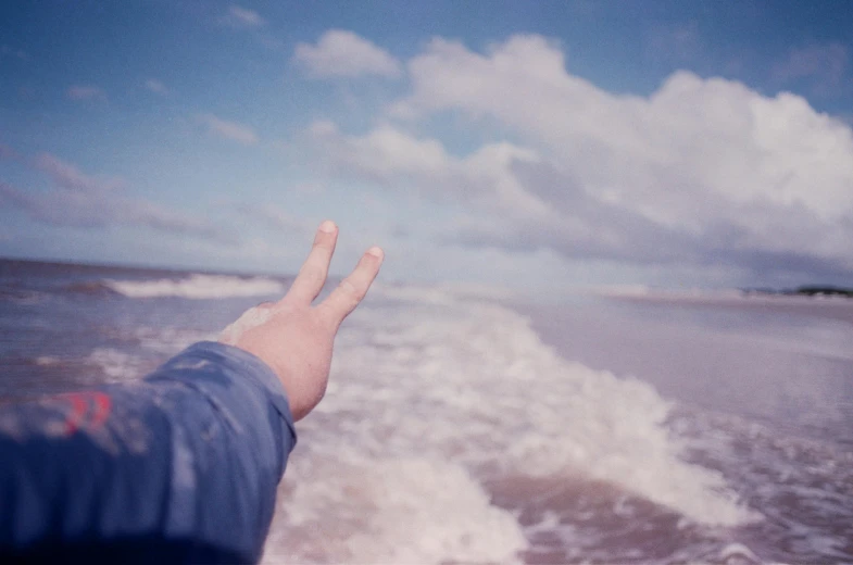 a person standing on top of a beach next to the ocean, an album cover, unsplash, land art, giving the middle finger, pastelwave, coherent hands, the photo was taken from a boat