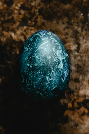 a blue stone sitting on top of a brown surface, by Adam Marczyński, trending on pexels, renaissance, magic frozen ice phoenix egg, carved black marble, easter, teal skin