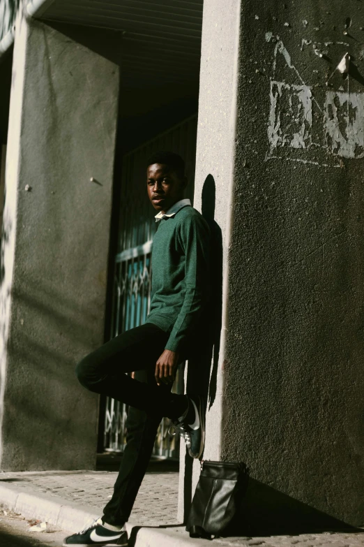 a man sitting on a chair in front of a building, an album cover, pexels contest winner, renaissance, in a dark green polo shirt, black teenage boy, wearing a green sweater, medium format. soft light