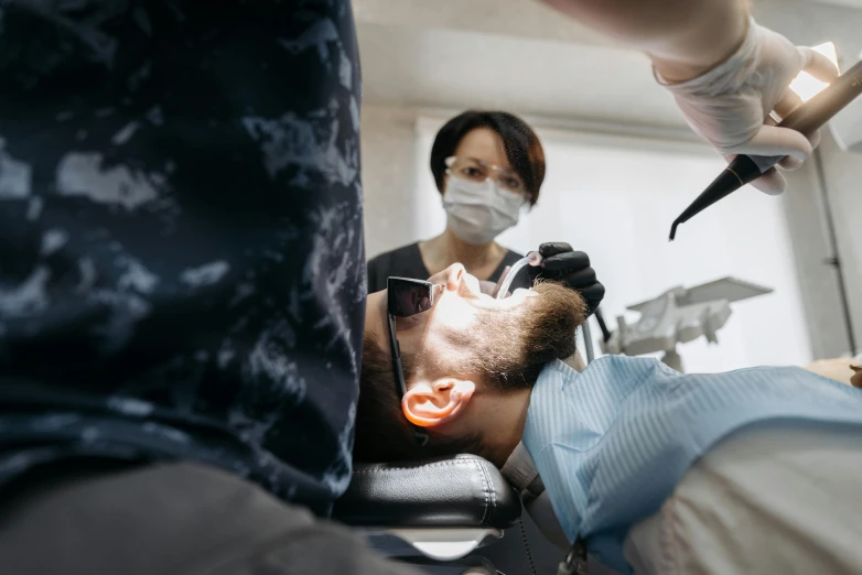 a man getting his teeth examined by a dentist, by Adam Marczyński, pexels contest winner, square masculine jaw, people are wearing masks, shaved face, falling out of the face