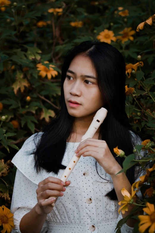 a woman standing in a field of yellow flowers, an album cover, inspired by Ruth Jên, pexels contest winner, realism, young girl playing flute, holding a wood piece, indonesia, ivory carved ruff