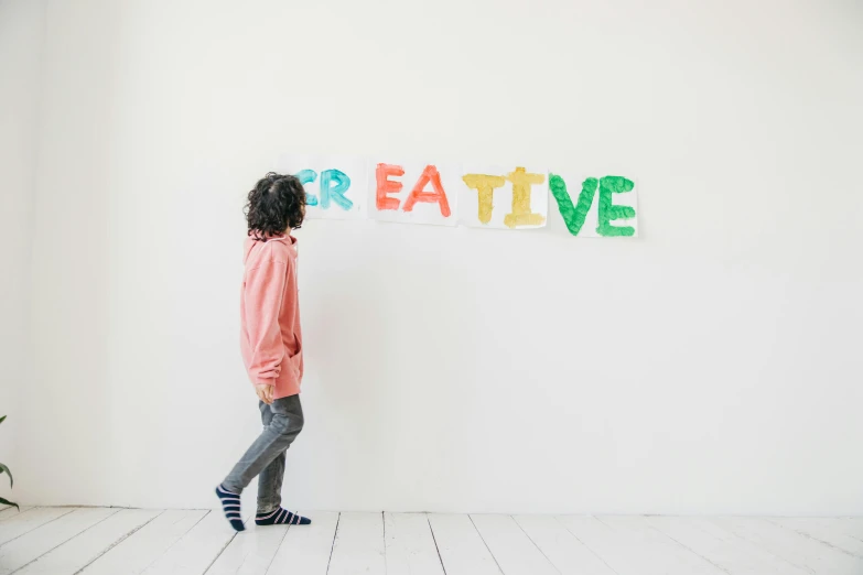 a little girl standing in front of a sign that says creative, an album cover, inspired by Peter de Sève, trending on unsplash, interactive art, white wall coloured workshop, tissue paper art, kids playing, studio shoot