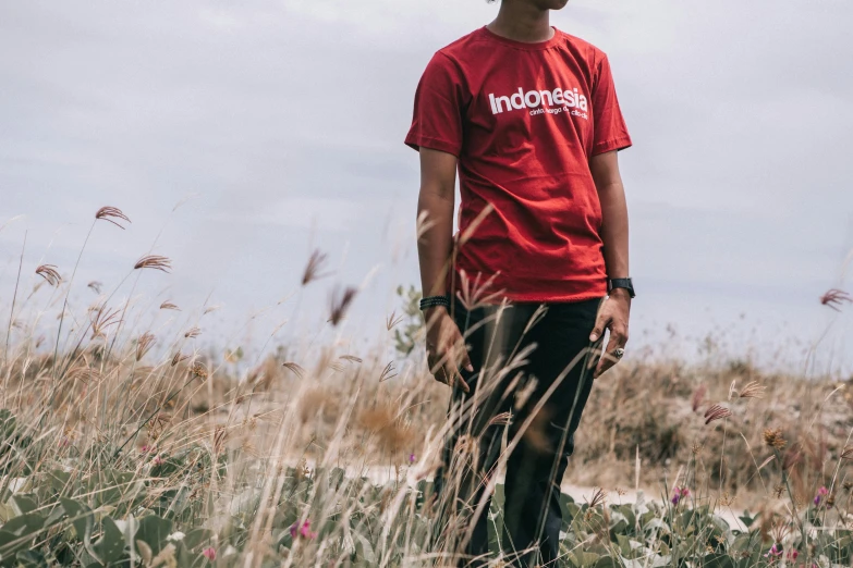 a man standing in a field of tall grass, inspired by Erik Pevernagie, unsplash, sumatraism, red t-shirt, streetwear, standing on rocky ground, it idn't greasy