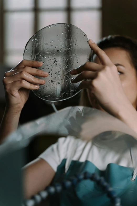 a woman holding a clock in front of her face, by Adam Marczyński, plasticien, filling with water, in a workshop, 8 k film still, teenage girl