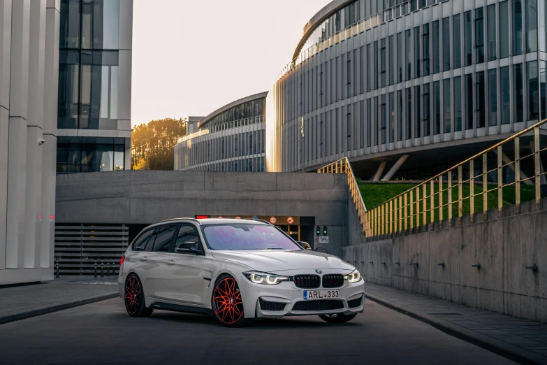 a white car driving down a street next to tall buildings, inspired by Jan Kupecký, pexels contest winner, renaissance, “2019 bmw m5 wagon, red rim light, in front of a garage, vray render 4 k