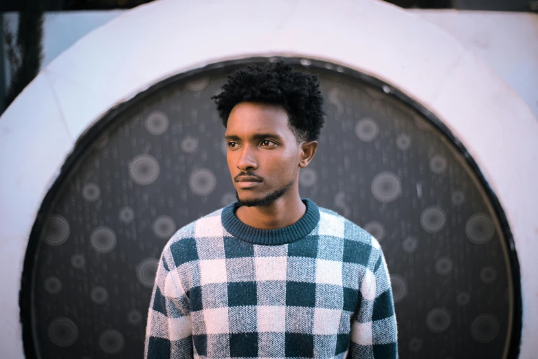 a man standing in front of a circular object, inspired by Afewerk Tekle, pexels contest winner, hurufiyya, wearing a sweater, checkered spiked hair, ethiopian, a handsome man，black short hair