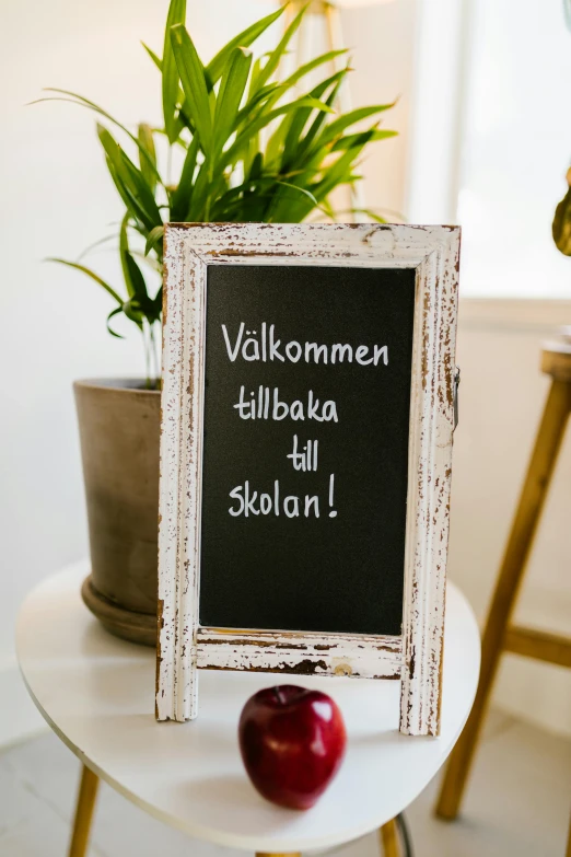a chalk board sitting on top of a table next to a potted plant, by Haukur Halldórsson, red apple, welcoming, shkkeled in the voied, dall - e