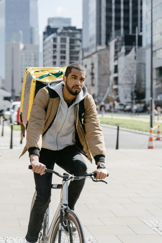 a man riding a bike down a city street, wearing a yellow hoodie, food, wearing a flying jacket, cardboard