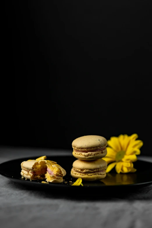 a black plate topped with macarons next to a yellow flower, a portrait, unsplash, smoked layered, very crispy, full product shot, caramel