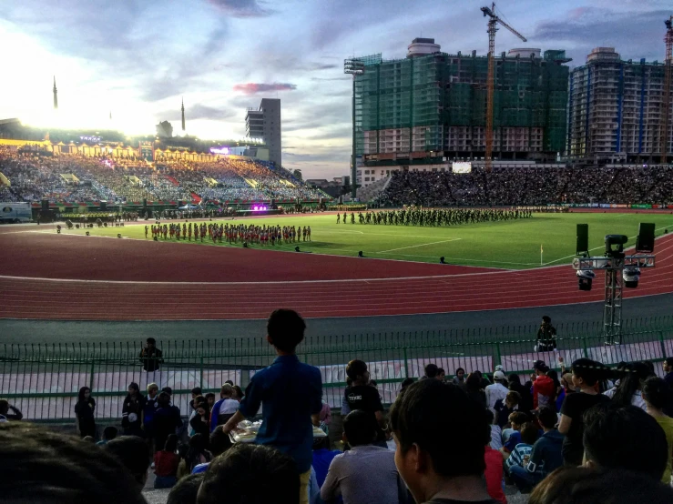 a group of people standing on top of a field, stadium full of people, malaysian, hoang lap, high light on the left