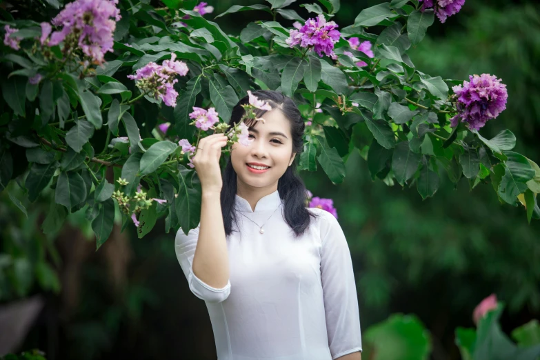 a woman standing in front of a tree with purple flowers, inspired by Cui Bai, pexels contest winner, white sleeves, young cute wan asian face, background image, vietnam