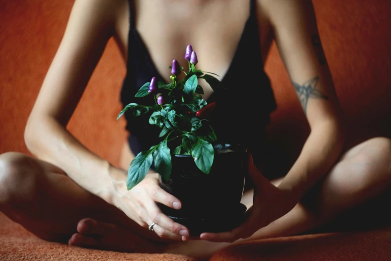 a woman sitting on a couch holding a potted plant, inspired by Elsa Bleda, trending on pexels, fine art, purple body, wearing a black bodysuit, flower buds, anjali mudra