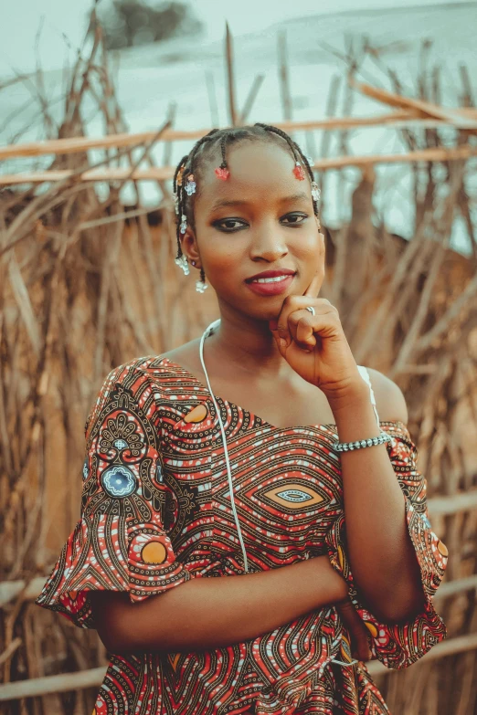 a woman standing in front of a wooden fence, by Chinwe Chukwuogo-Roy, pexels contest winner, afrofuturism, wearing a dress made of beads, cute young woman, headshot, teenage girl