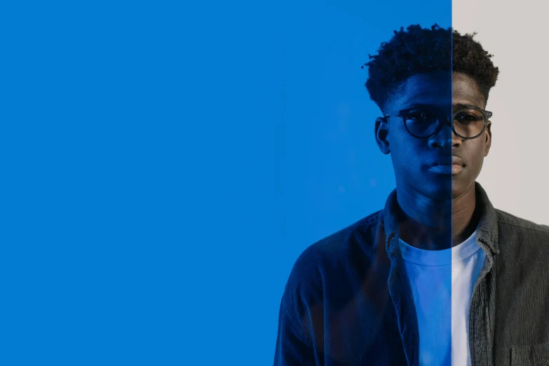 a man standing in front of a blue background, an album cover, by Frank Mason, trending on pexels, realism, black teenage boy, man with glasses, high blue lights, duotone