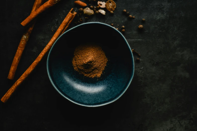 a blue bowl filled with spices next to two wooden spoons, by Julia Pishtar, pexels contest winner, sitting on a mocha-colored table, black and auburn colour pallet, dessert, avatar image