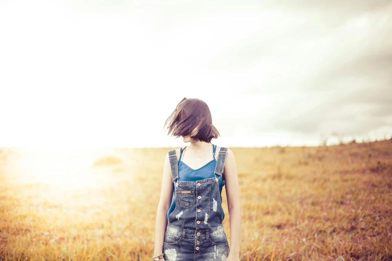 a woman standing in a field with a suitcase, unsplash, torn overalls, head turned, instagram picture, plain background