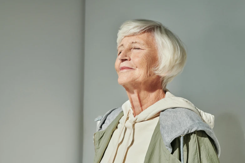 a woman standing in a room with her eyes closed, inspired by Sigrid Hjertén, unsplash, photorealism, elderly, plain background, looking upwards, calm weather
