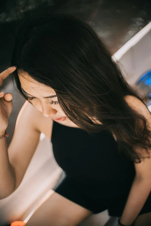 a woman holding a cell phone to her ear, trending on pexels, dark long hair, looking down, li zixin, she is wearing a black tank top