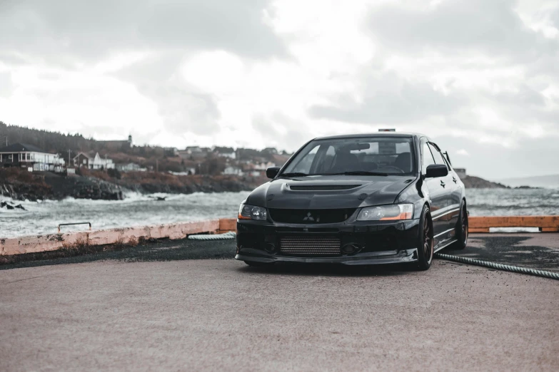 a black car parked in front of a body of water, pexels contest winner, extreme shitty car mods, jdm, on a cloudy day, front portrait