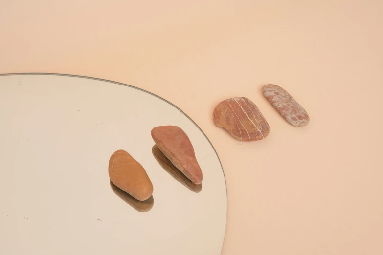 a mirror sitting on top of a table next to rocks, inspired by Isamu Noguchi, surrealism, brown and pink color scheme, miniature product photo, gemstones, tan