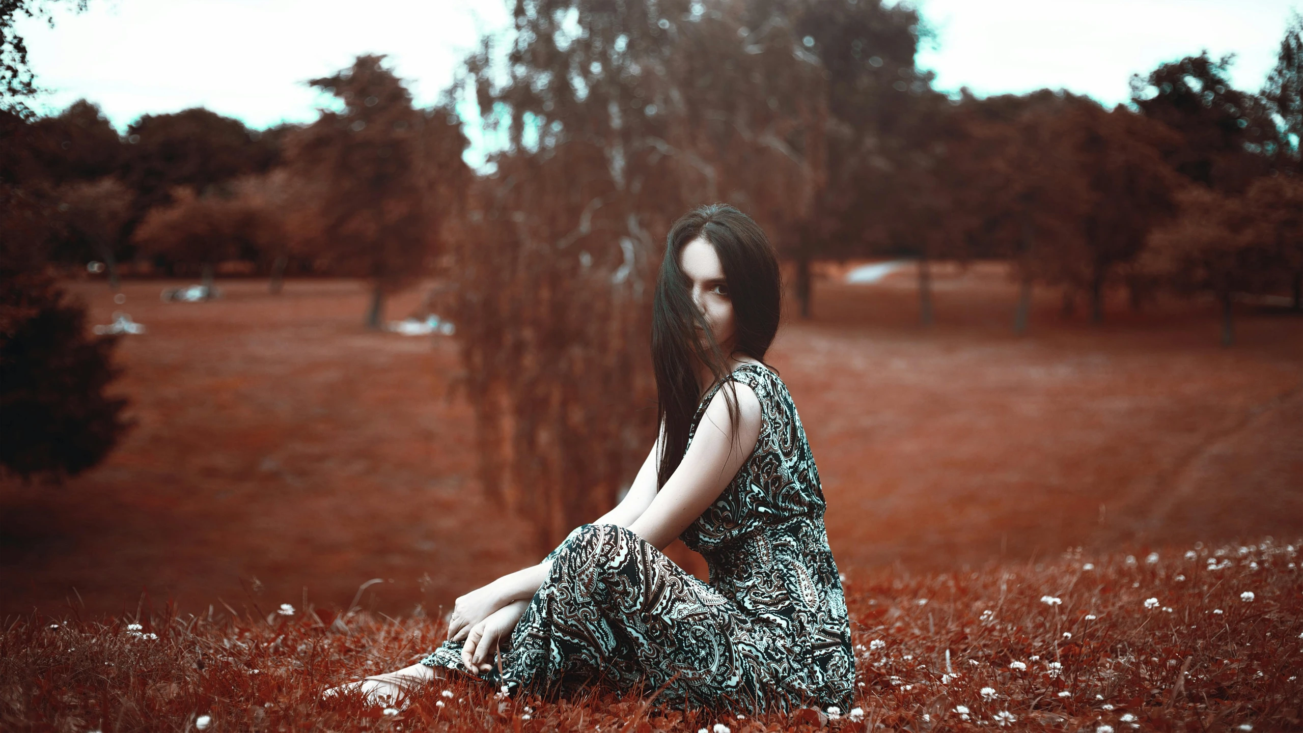 a woman sitting on top of a lush green field, a black and white photo, inspired by Elsa Bleda, pexels contest winner, red selective coloring, girl with dark brown hair, patterned clothing, pale - skinned