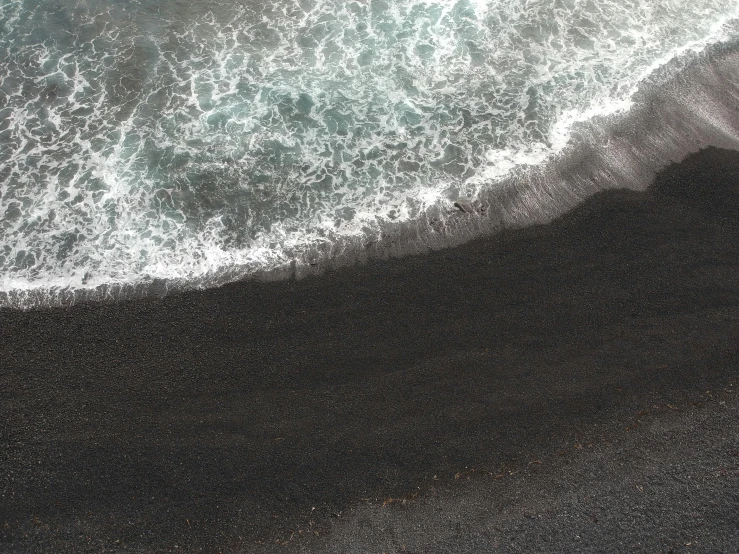 a person riding a surfboard on top of a black sand beach, inspired by Andreas Gursky, pexels contest winner, realism, sea foam, view from the sky, ignant, beach is between the two valleys