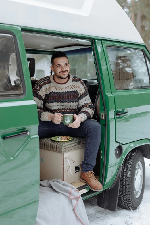 a man sitting in the back of a green van, food. craft and adventure, dressed in 1970s menswear, winter setting, promo image