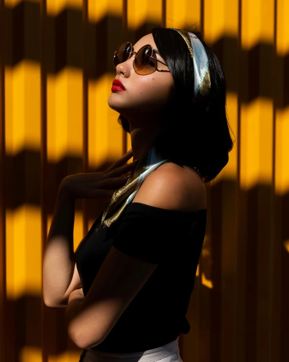 a woman standing in front of a yellow wall, an album cover, by Julia Pishtar, unsplash, dramatic backlit lighting, wearing versace sunglasses, an asian woman, standing under a beam of light