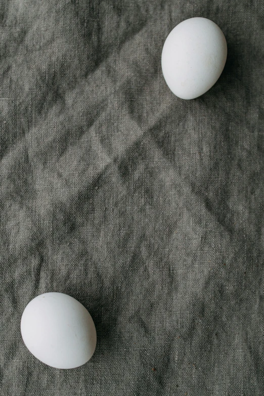 three white eggs sitting on top of a table, by Carey Morris, trending on unsplash, grey cloth, repeating pattern, linen, long