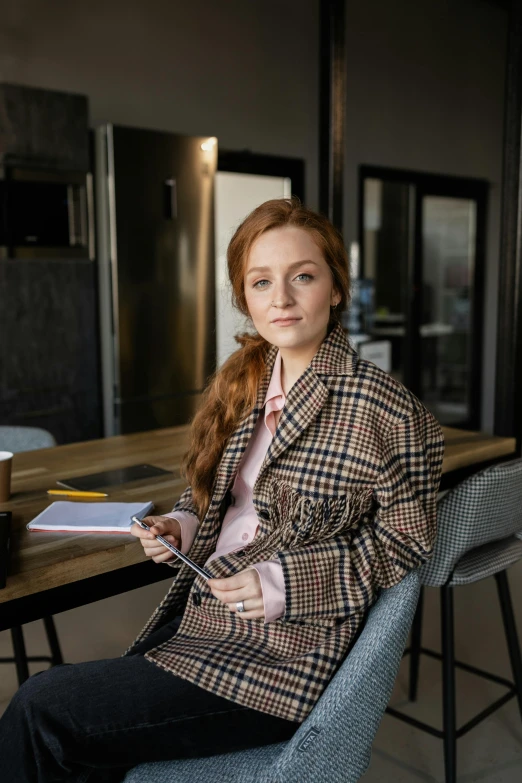 a woman sitting at a table with a cup of coffee, wearing a blazer, a redheaded young woman, taken in 2 0 2 0, abcdefghijklmnopqrstuvwxyz