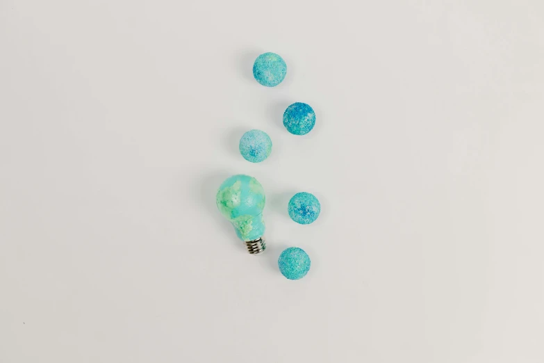 a light bulb sitting on top of a white table, inspired by Évariste Vital Luminais, process art, blue and green, candy decorations, detailed product photo, sea foam