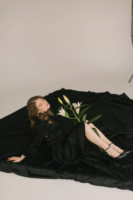 a woman in a black dress laying on a black blanket, an album cover, unsplash, lillies, full body full height, ignant, at a fashion shoot