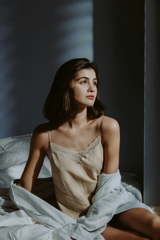 a woman sitting on top of a bed covered in sheets, inspired by Elsa Bleda, trending on pexels, renaissance, wearing a camisole, thoughtful expression, with high cheekbones, linen