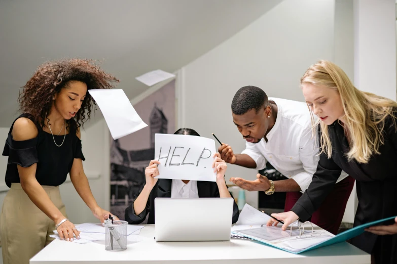 a group of people standing around a table with a laptop, struggling, woman holding sign, professional image, multiple stories